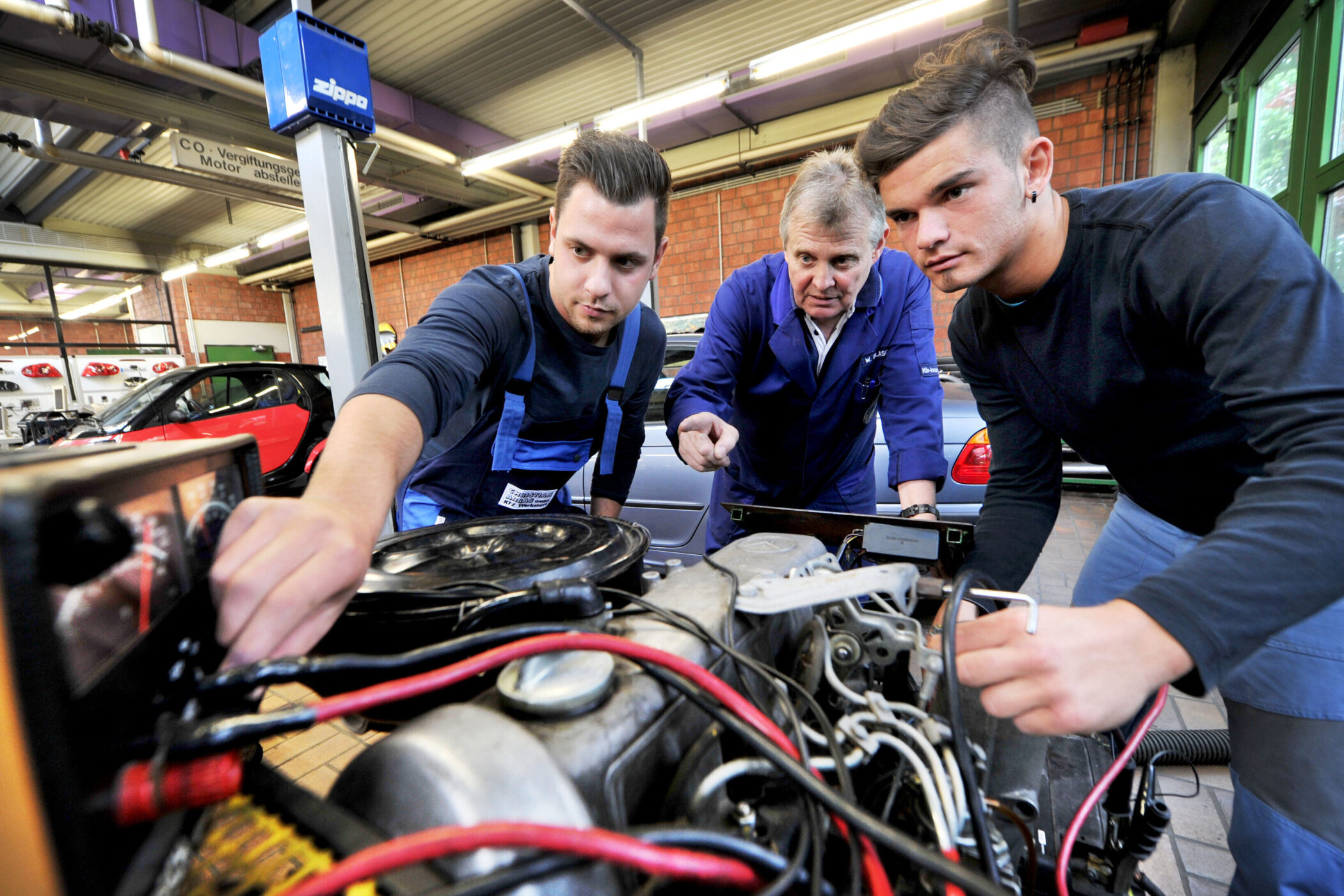 Drei Personen arbeiten an einem Motor in einer Werkstatt.