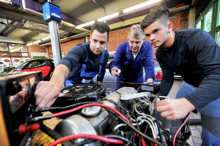 Drei Personen arbeiten an einem Motor in einer Werkstatt.