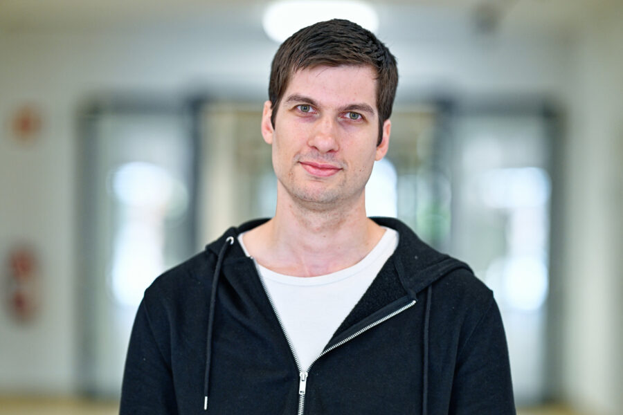 Eine Person mit dunklen Haaren in schwarzer Kapuzenjacke, unscharfer Hintergrund.