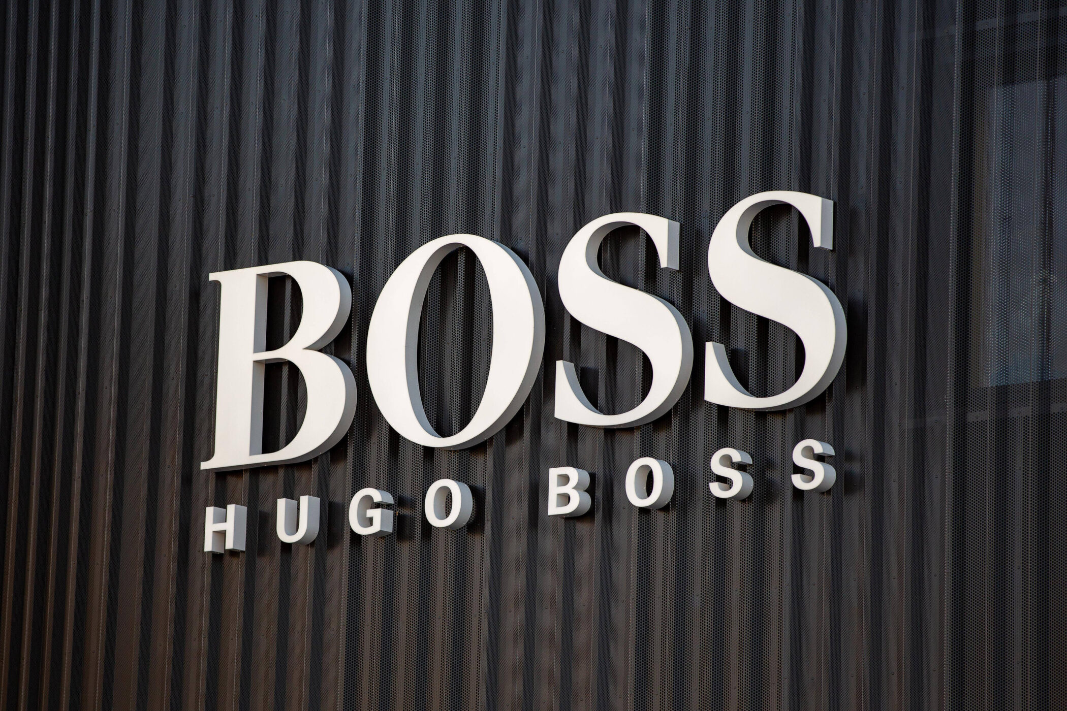 Weiße Buchstaben "BOSS HUGO BOSS" auf geriffeltem, dunklem Hintergrund.