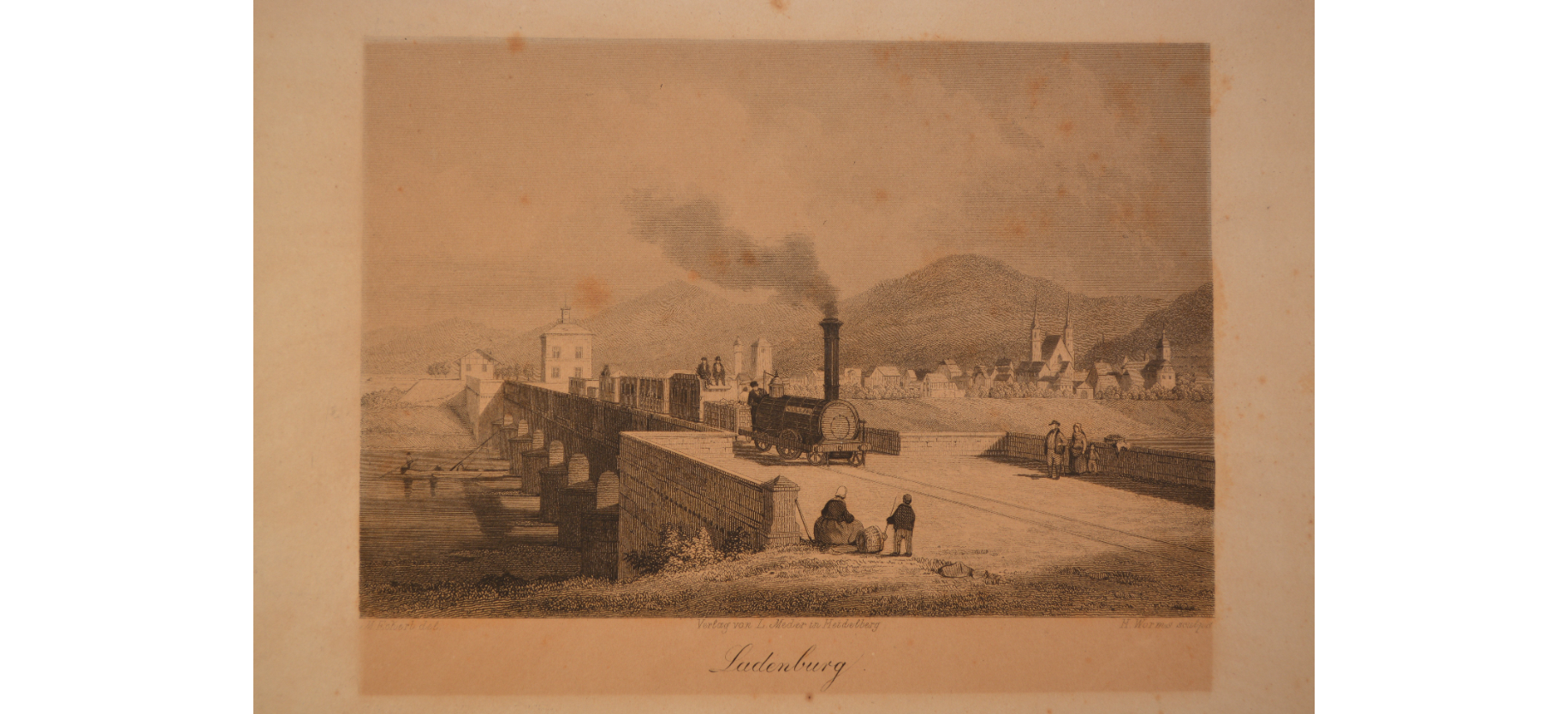 Zug auf Brücke, zwei Personen sitzen, Dorf und Hügel im Hintergrund, Text: „Ladenburg“.