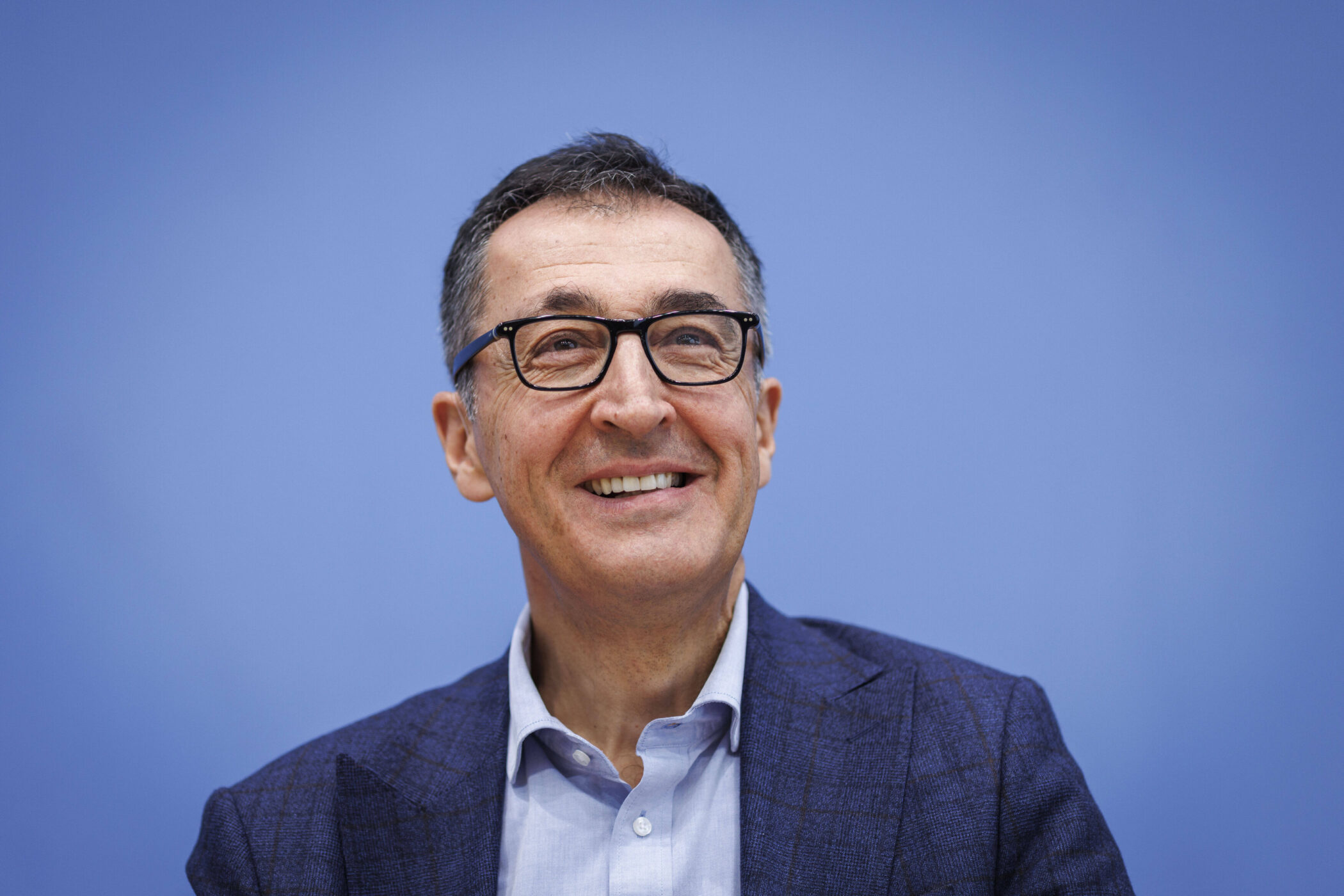 Mann mit Brille und Anzug vor blauem Hintergrund, lächelnd.