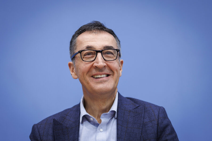 Mann mit Brille und Anzug vor blauem Hintergrund, lächelnd.
