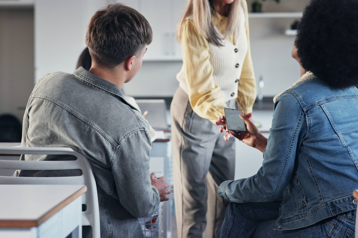 Drei Personen unterhalten sich, eine zeigt auf ein Smartphone.