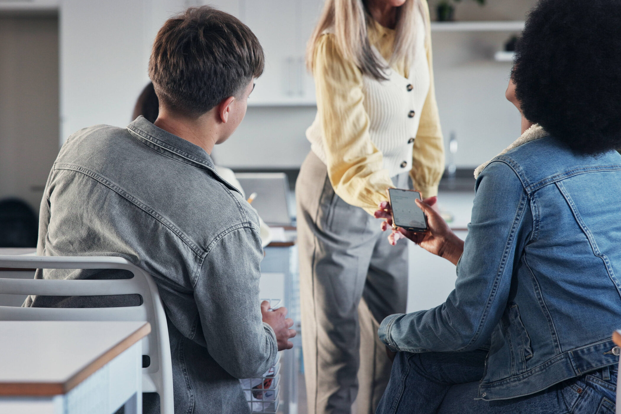 Drei Personen unterhalten sich, eine zeigt auf ein Smartphone.