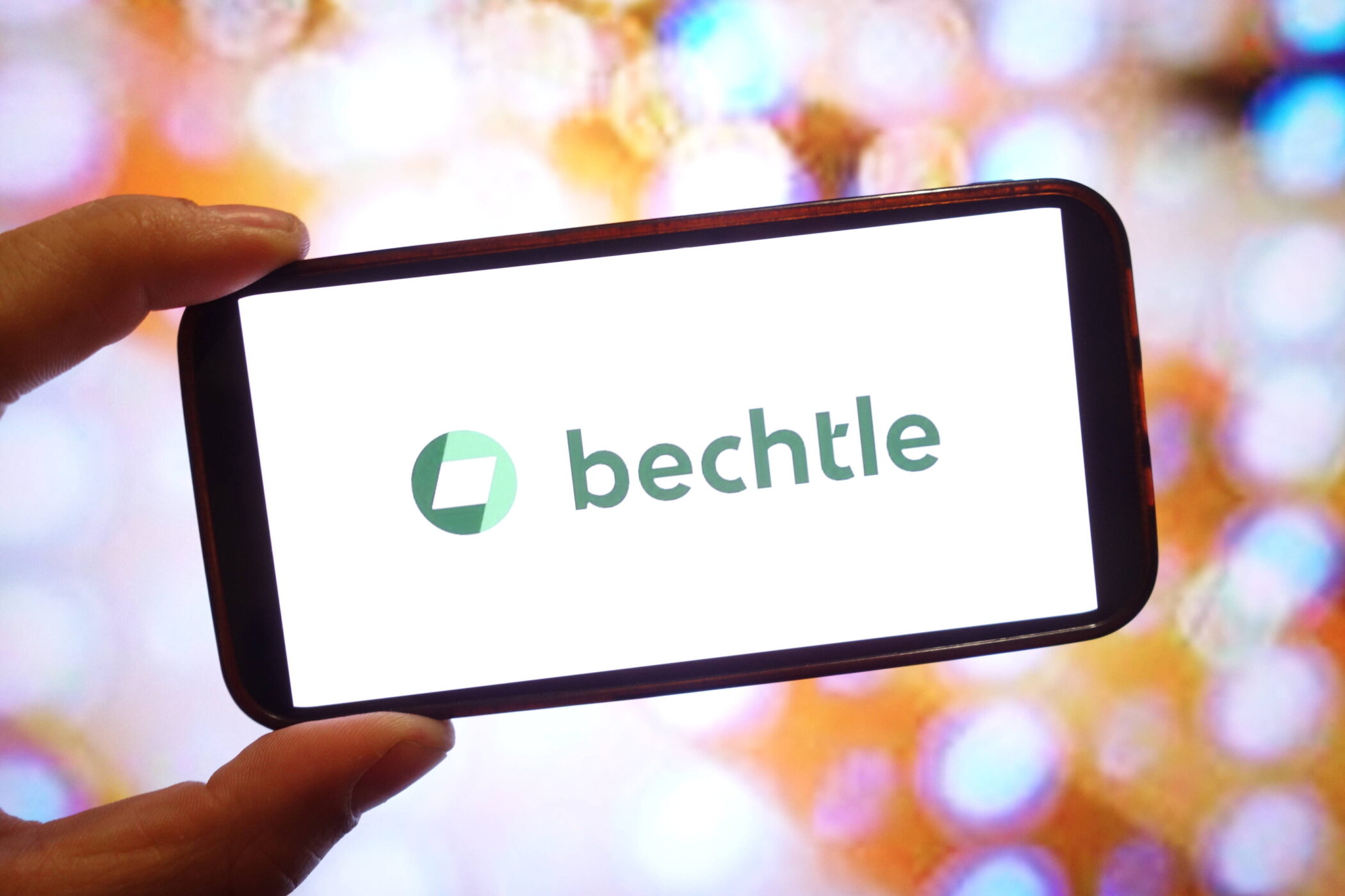 Hand hält ein Smartphone mit Bechtle-Logo auf weißem Bildschirm. Bunte Lichter im Hintergrund.
