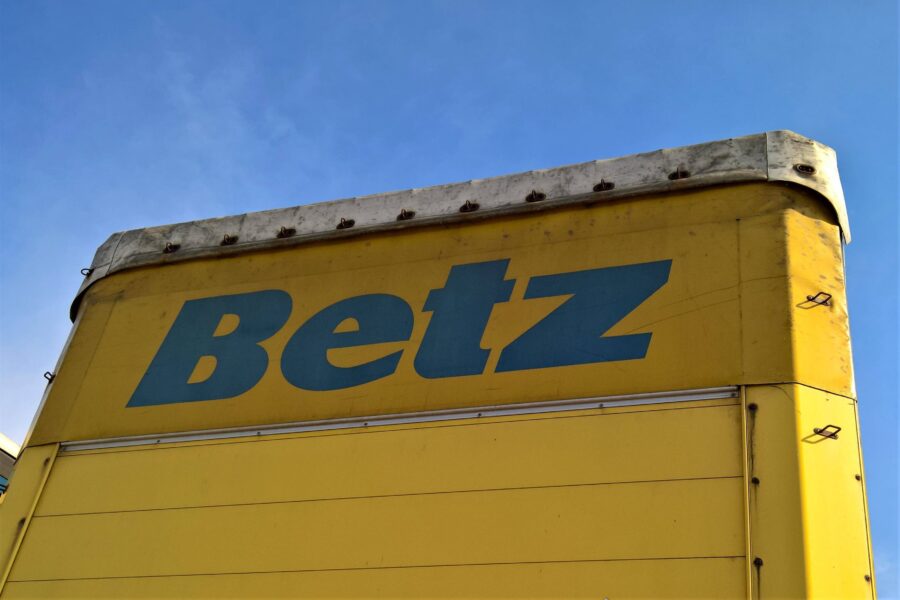Gelber Lastwagen mit blauem Schriftzug "Betz" vor blauem Himmel.