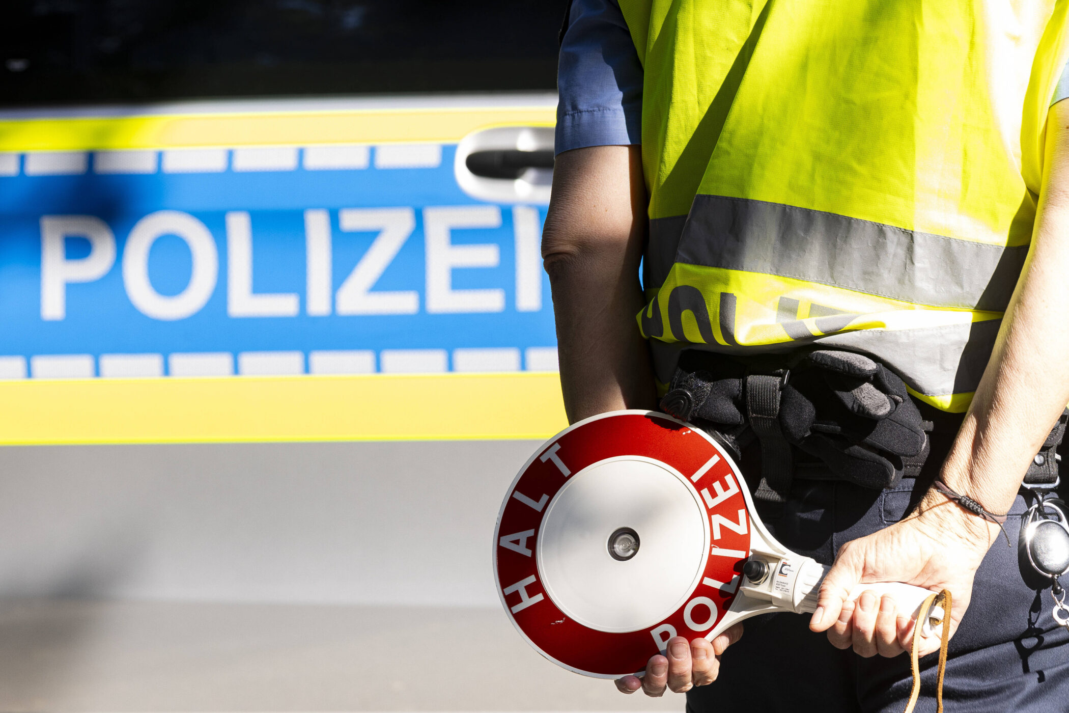Person mit Warnweste hält Kelle "Halt Polizei" vor Polizeifahrzeug.