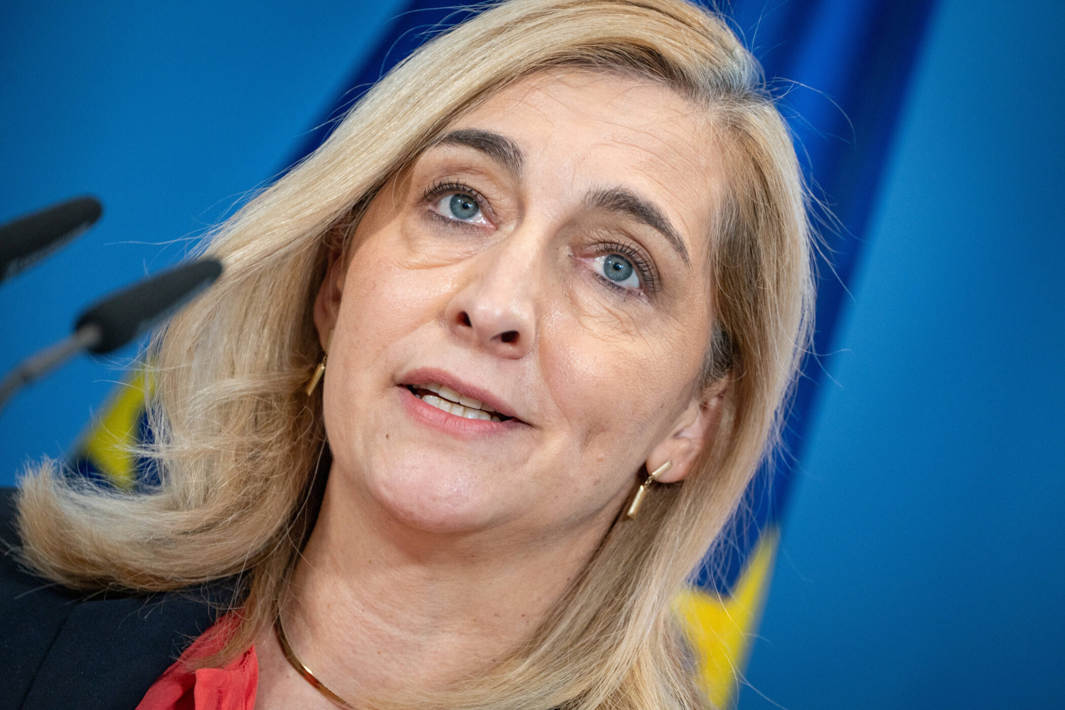 Eine Frau mit blonden Haaren vor blauem Hintergrund mit Mikrofon.