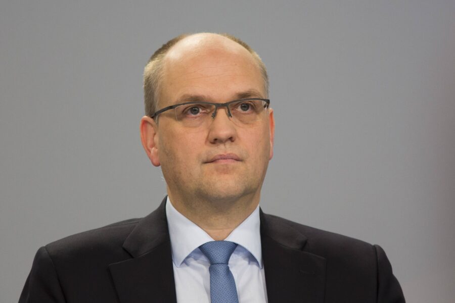 Ein Mann mit Brille und Anzug vor grauem Hintergrund.