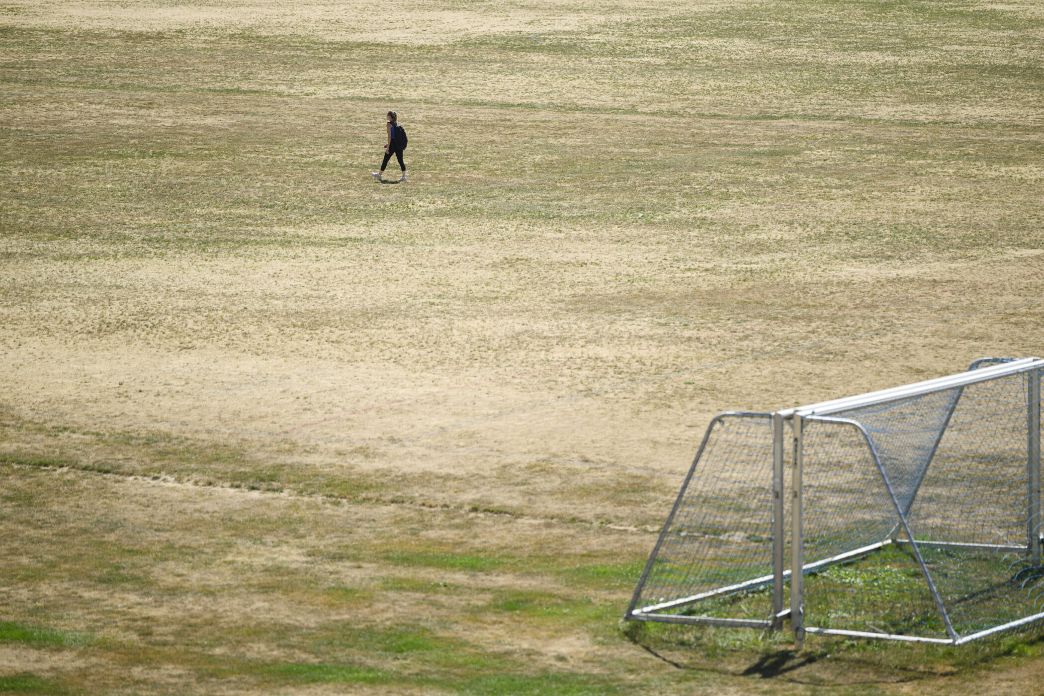 Eine Person geht über ein trockenes Feld, rechts ein Fußballtor.