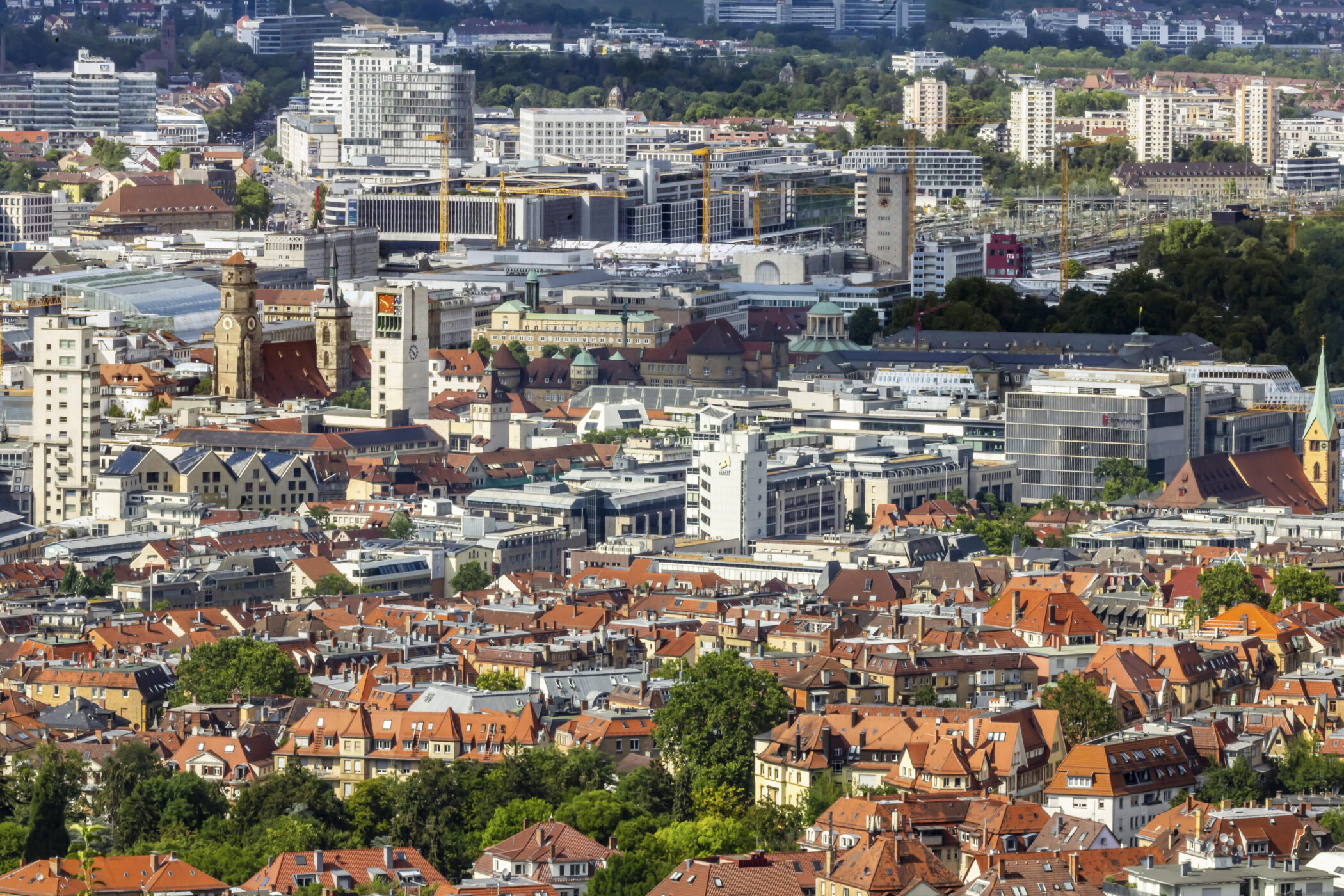 Stadtansicht mit roten Dächern, hohen Gebäuden und Turm im Zentrum, im Hintergrund Wald.