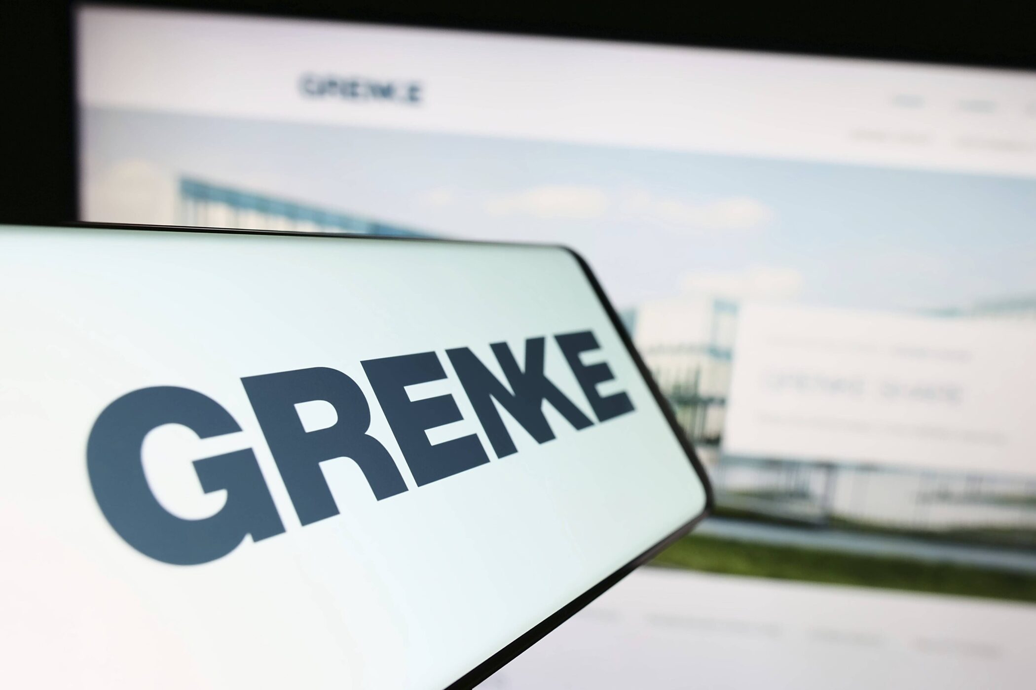 Text "GRENKE" groß auf einem Bildschirm, unscharfer Hintergrund.