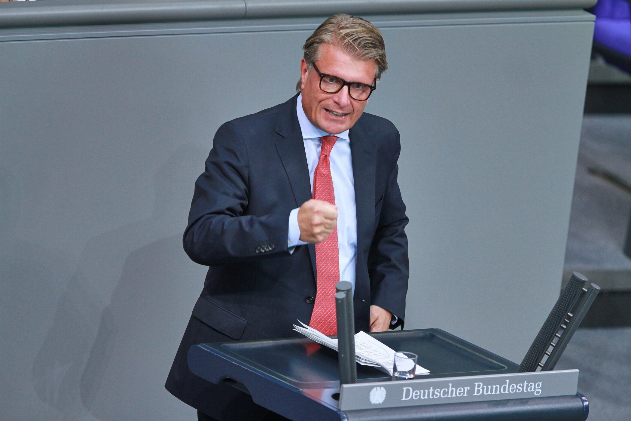 Ein Mann im Anzug spricht an einem Rednerpult mit Aufschrift "Deutscher Bundestag".