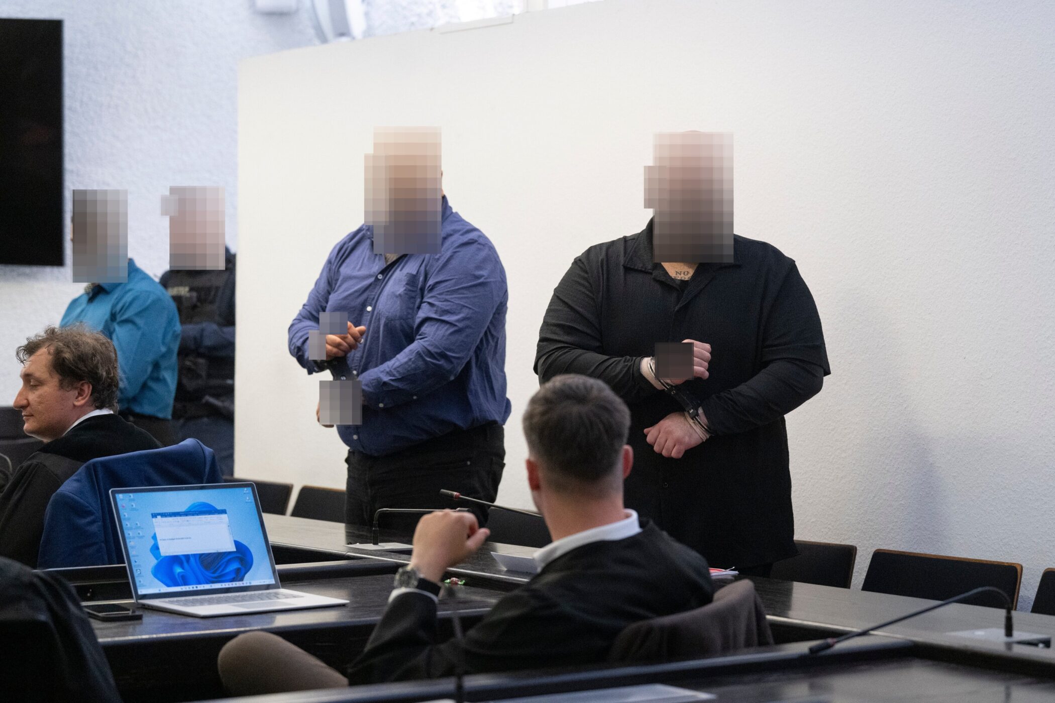 Mehrere Personen in einem Raum, einige stehen, einer sitzt vor einem Laptop.