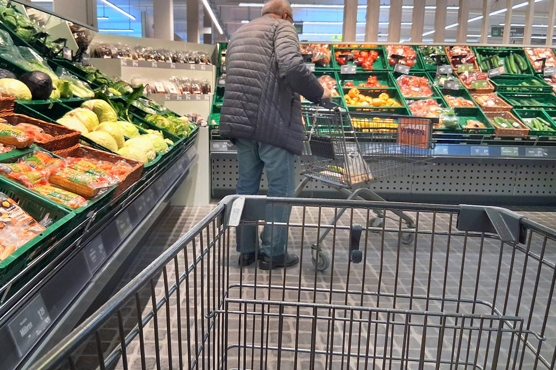 Ein Mann steht mit Einkaufswagen vor Gemüseauslage im Supermarkt.