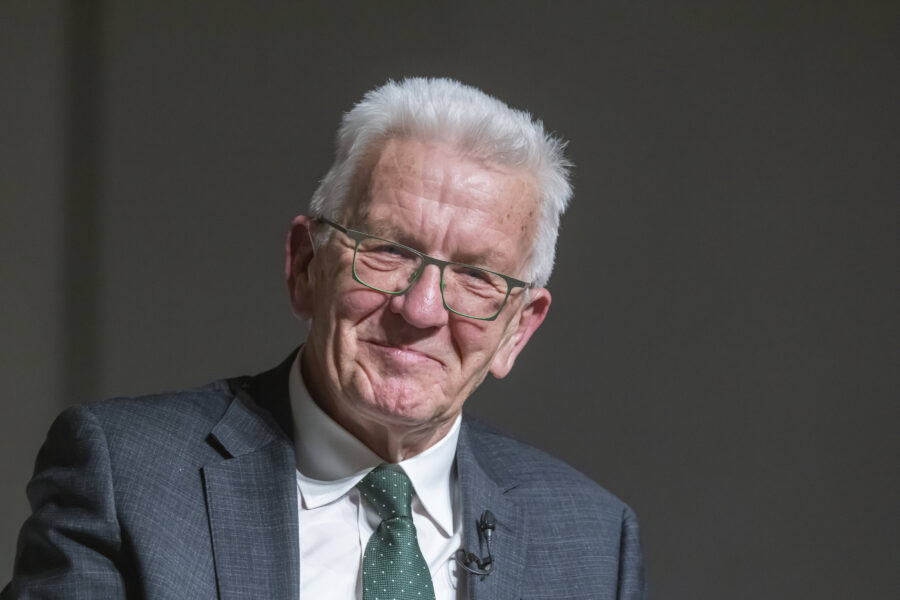 Älterer Mann mit weißem Haar und Brille im Anzug, lächelnd.