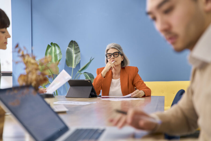 Drei Personen bei einem Meeting, eine Person konzentriert, mit Tablet und Dokumenten.