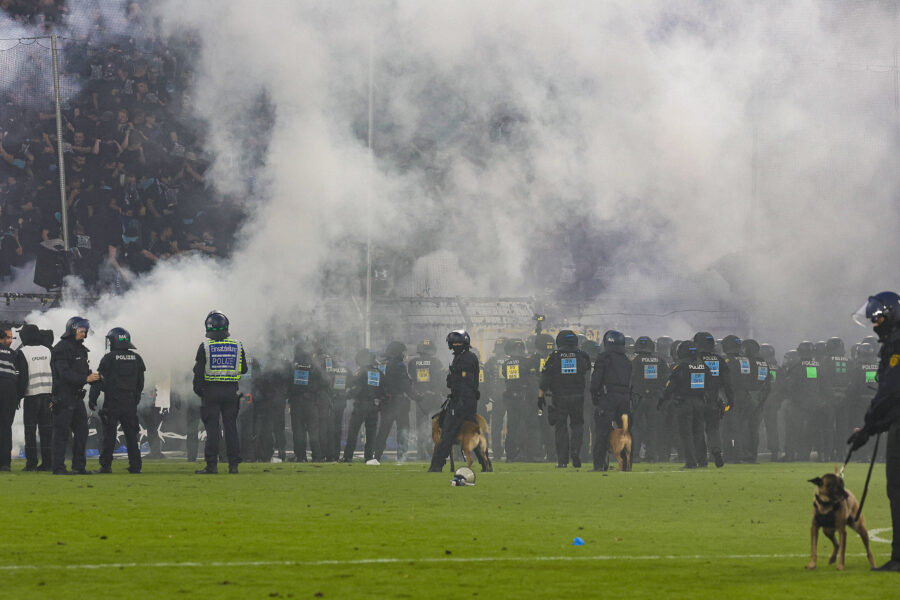 Polizisten mit Hunden und Rauch vor einer Menschenmenge im Stadion.