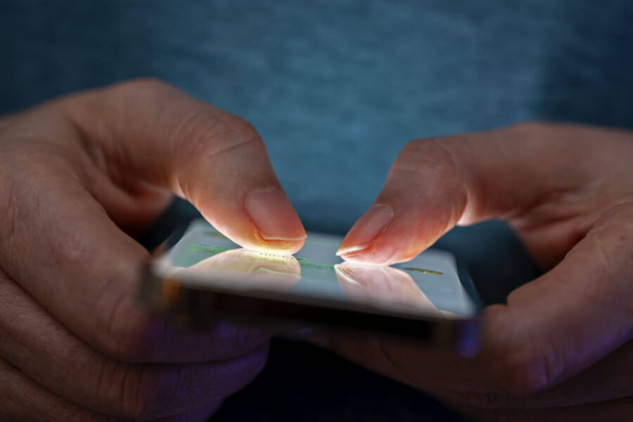 Person tippt mit beiden Daumen auf einem Smartphone mit beleuchtetem Display.