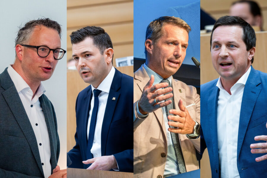 Vier Männer in Anzügen, sprechen jeweils in Mikrofone.