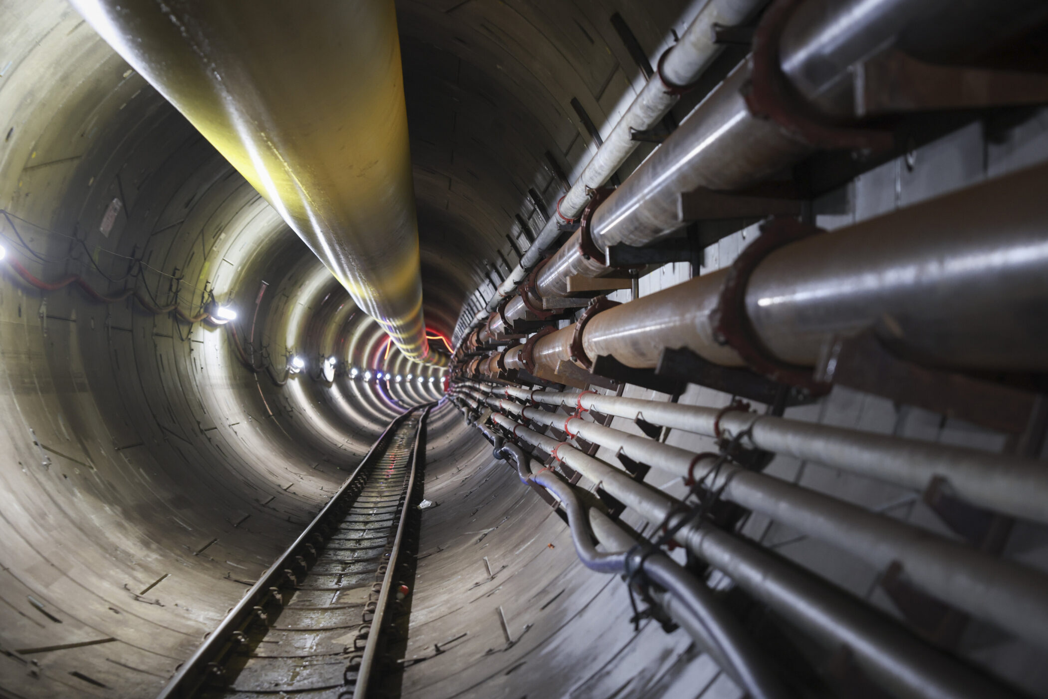 Rundes Tunnelinnere mit Schienen und Rohren an den Wänden.