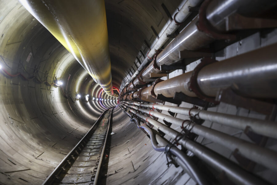 Rundes Tunnelinnere mit Schienen und Rohren an den Wänden.