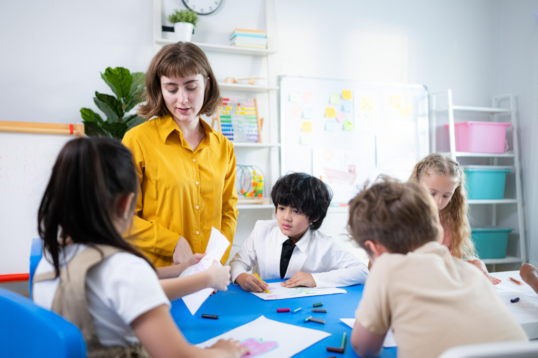 Lehrerin spricht mit fünf Kindern, die an einem Tisch malen.