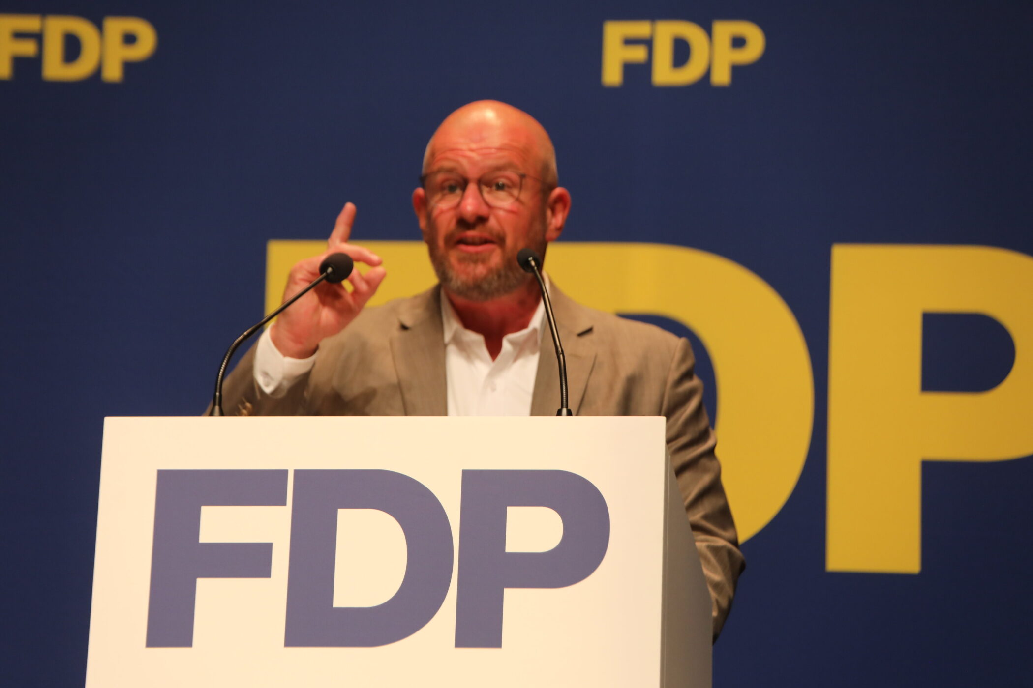 Eine Person spricht an einem Pult mit FDP-Logo, Hintergrund blau mit gelbem FDP-Schriftzug.