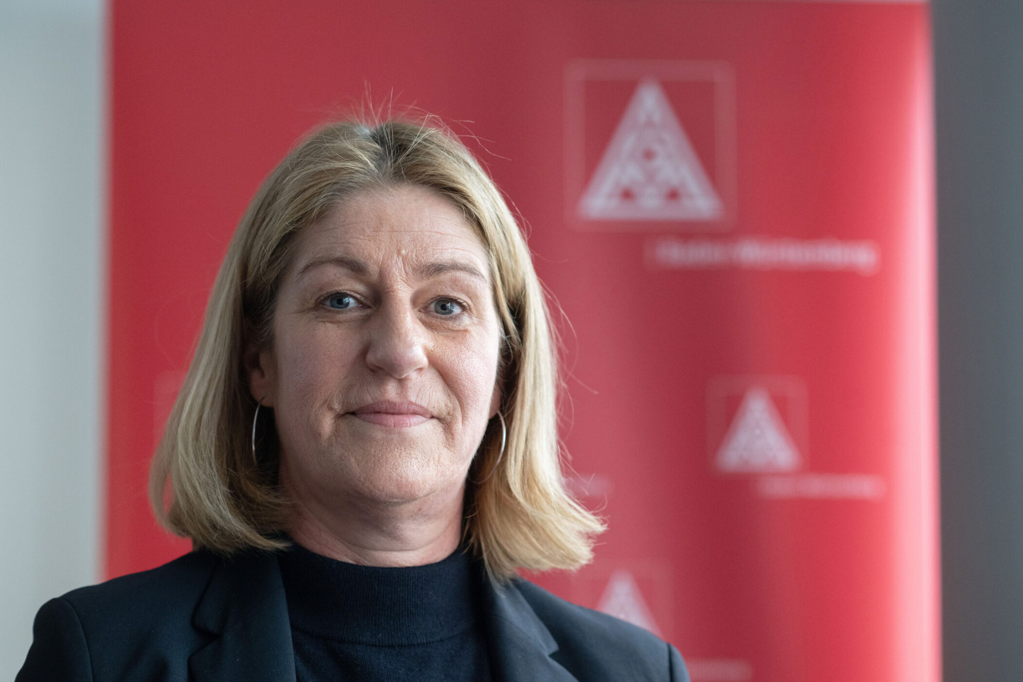 Eine Frau vor einem roten Hintergrund mit einem weißen Logo.