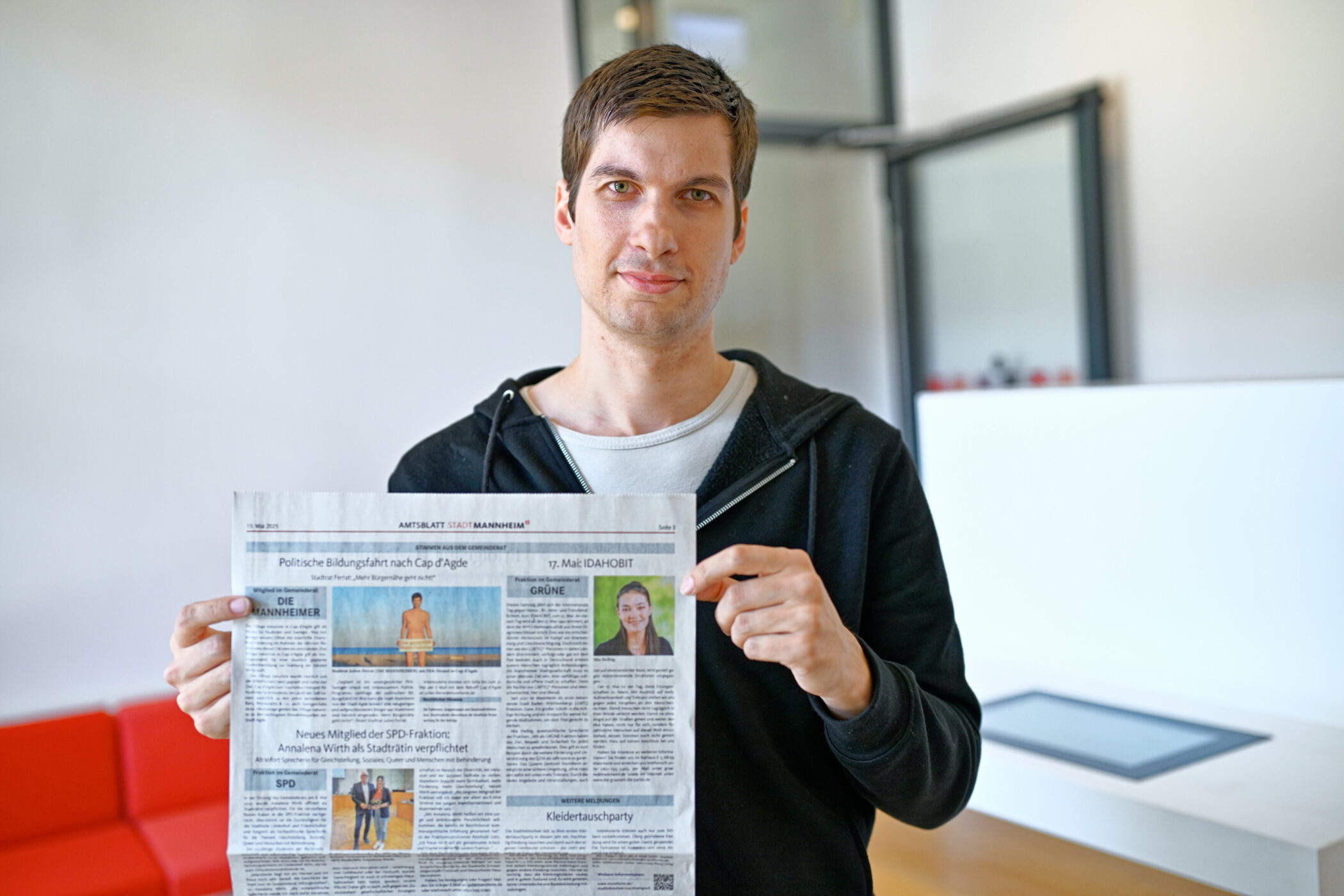 Mann hält eine Zeitung; Überschrift: "Politische Bildungsfahrt nach Cap d'Agde".