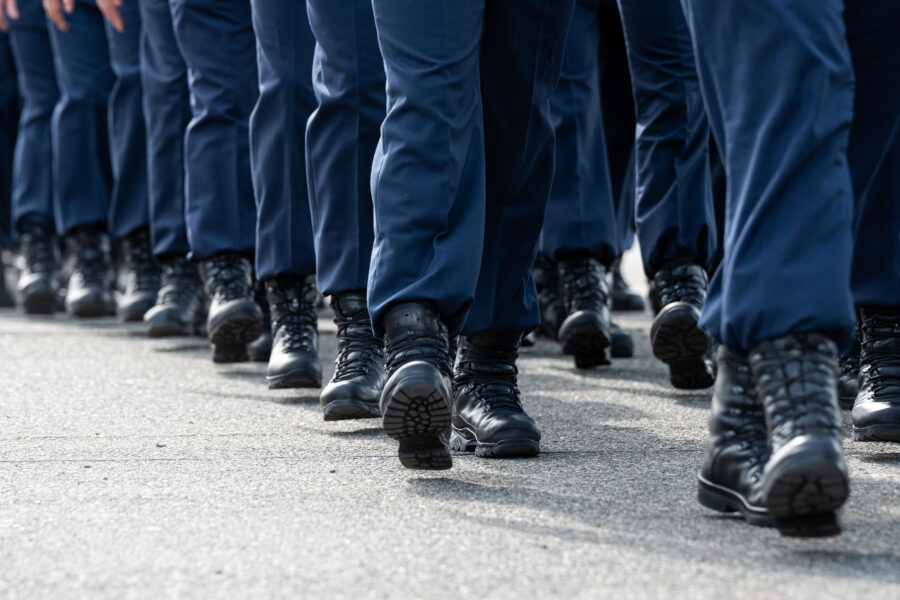 Mehrere Personen in Uniformhosen und Stiefeln marschieren auf einer Straße.