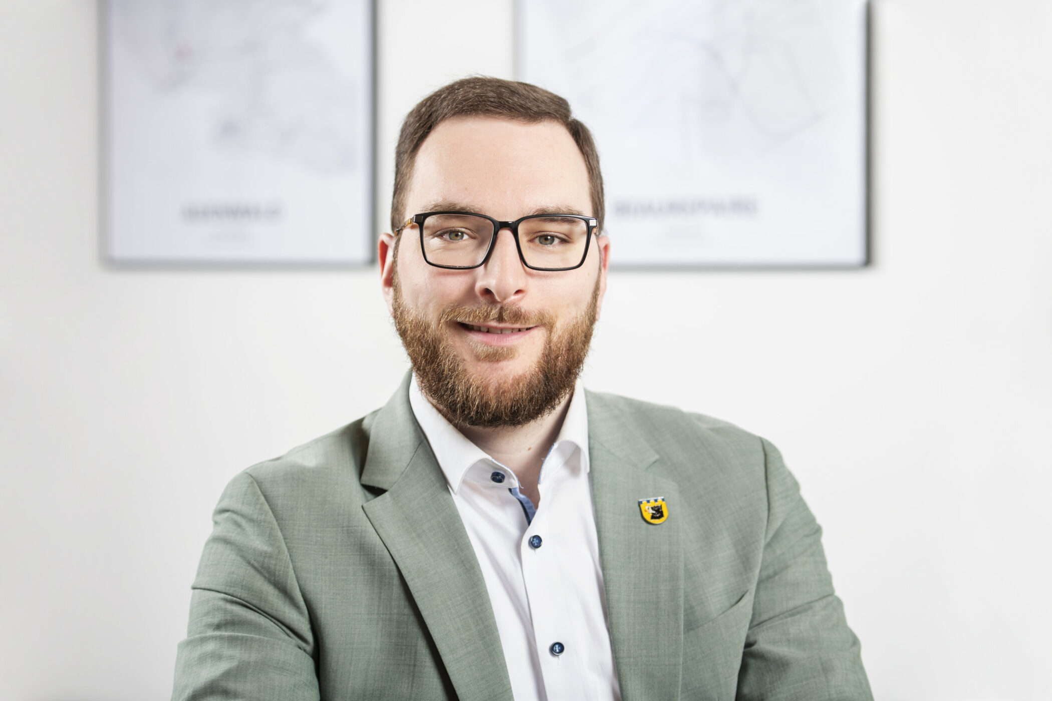 Mann mit Brille im Anzug, im Hintergrund unscharfe Wandbilder.