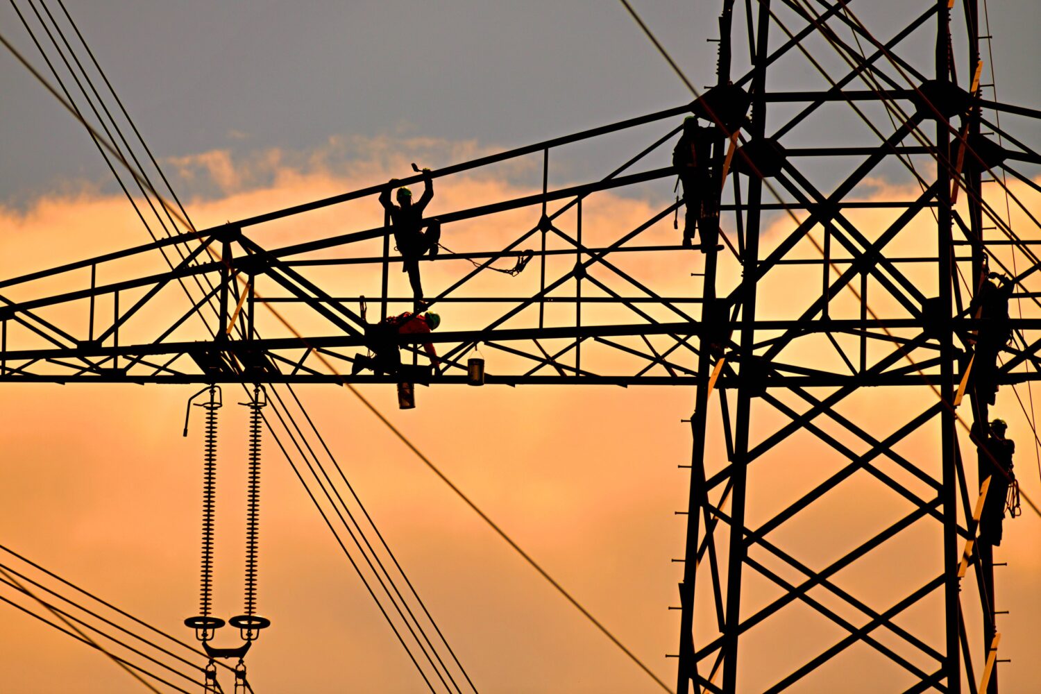 Vier Personen arbeiten auf einem Strommast bei Sonnenuntergang.