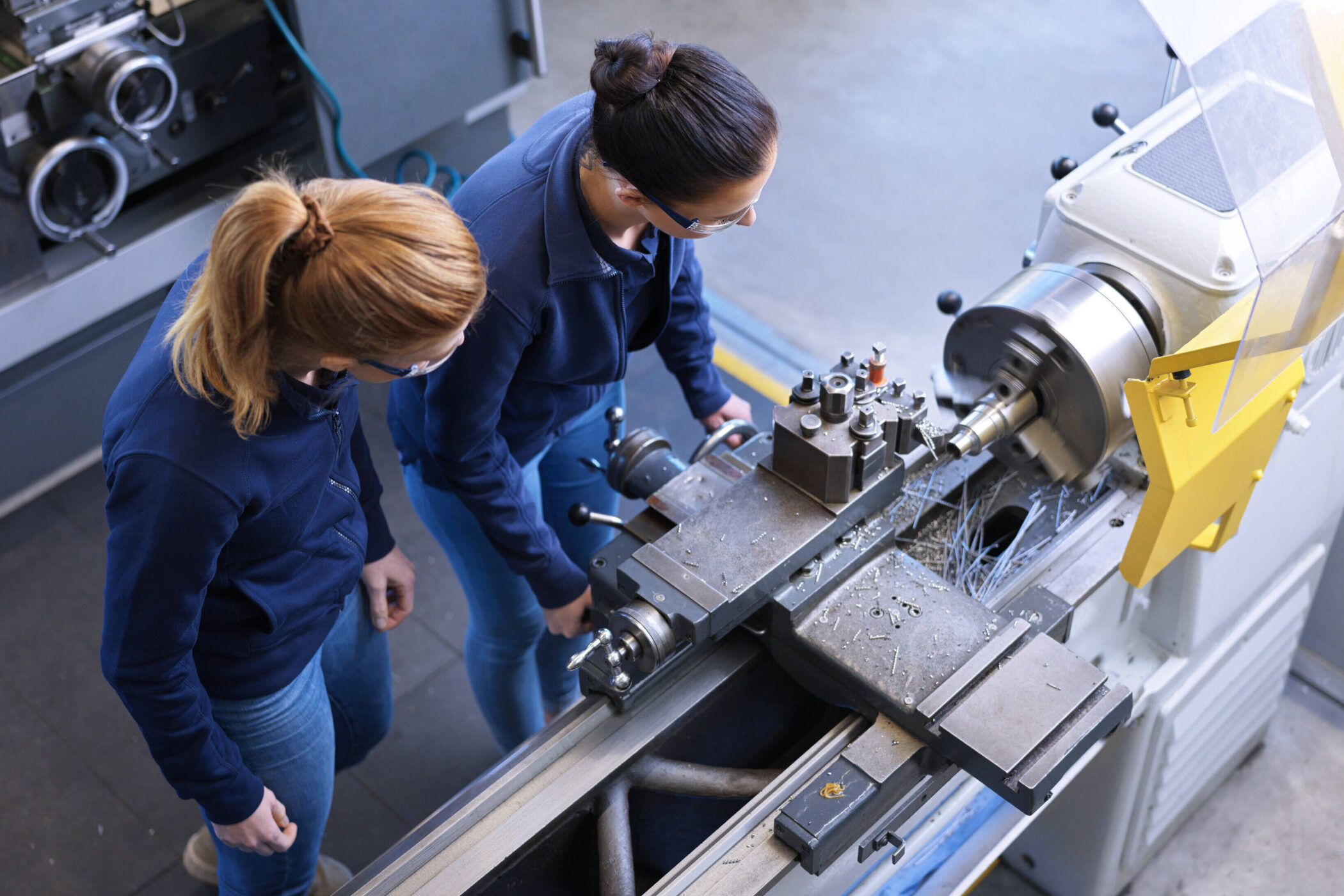 Zwei Personen bedienen eine Drehmaschine in einer Werkstatt.