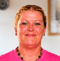 Person mit geflochtenem Haar und rosa Oberteil lächelt in die Kamera.