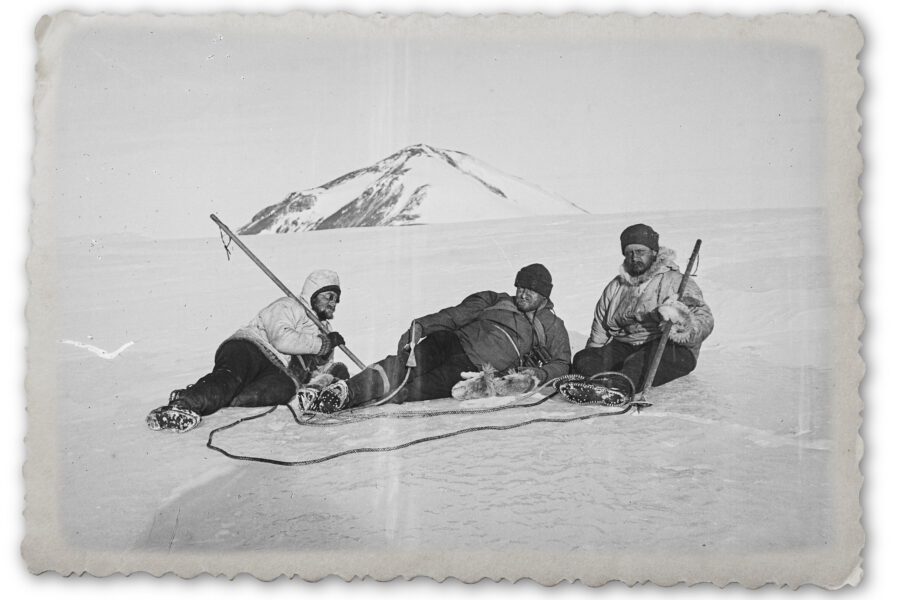 Drei Menschen sitzen auf einem schneebedeckten Feld vor einem Berg.