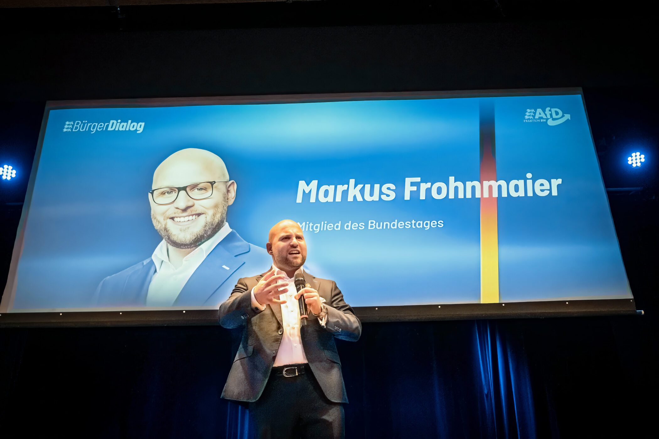 Ein Mann steht vor einer Leinwand mit Text "Markus Frohnmaier, Mitglied des Bundestages".