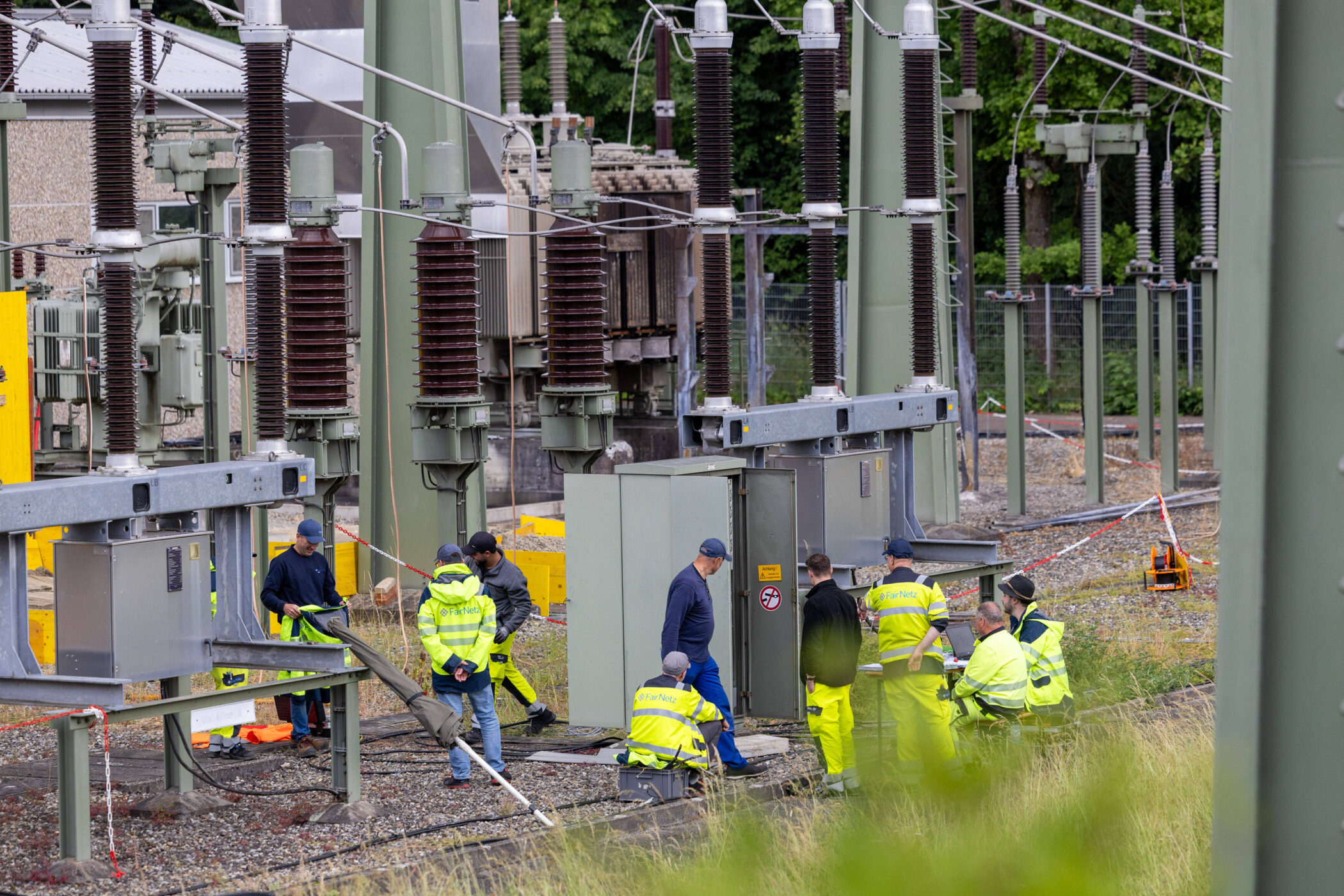 Mehrere Menschen in Schutzkleidung bei Arbeiten an Transformatorstation.