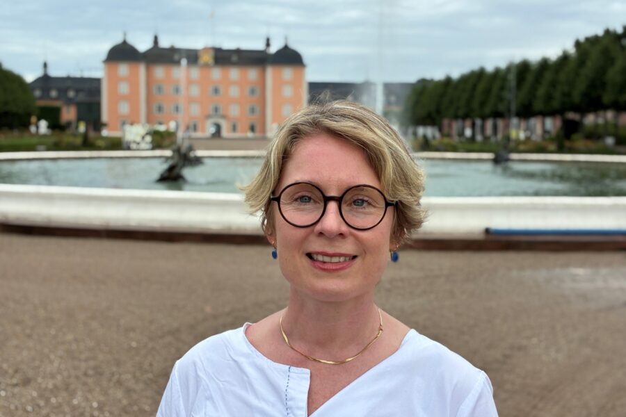 Eine Person mit Brille vor Schloss und Brunnen.