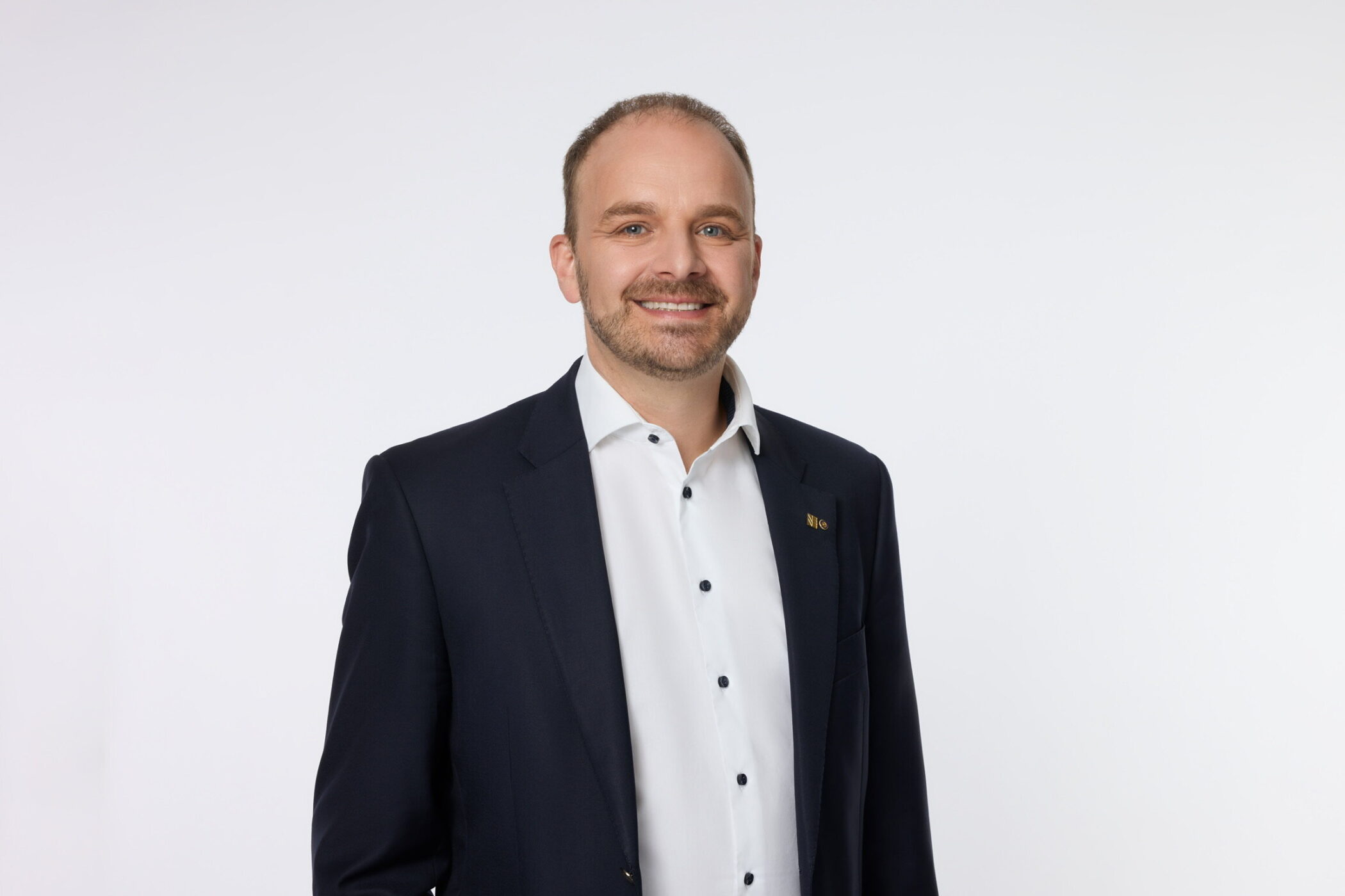 Ein Mann im Anzug lächelt vor weißem Hintergrund.