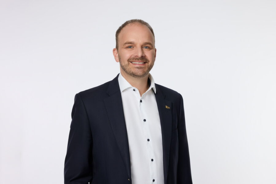 Ein Mann im Anzug lächelt vor weißem Hintergrund.