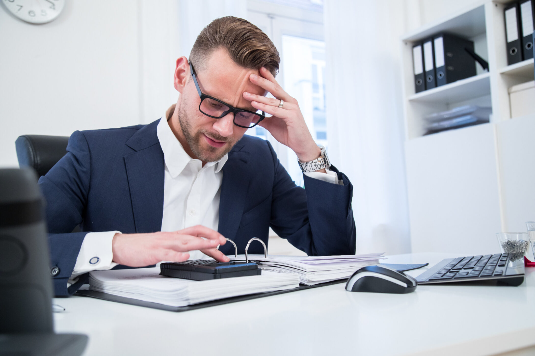 Person in Anzug, arbeitet mit Aktenordner und Taschenrechner am Schreibtisch.