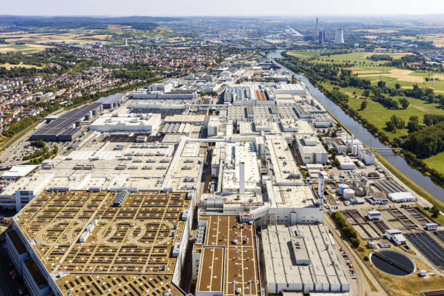 Luftaufnahme großer Industriekomplex mit begrünten Dächern, im Hintergrund Fluss und Stadt.