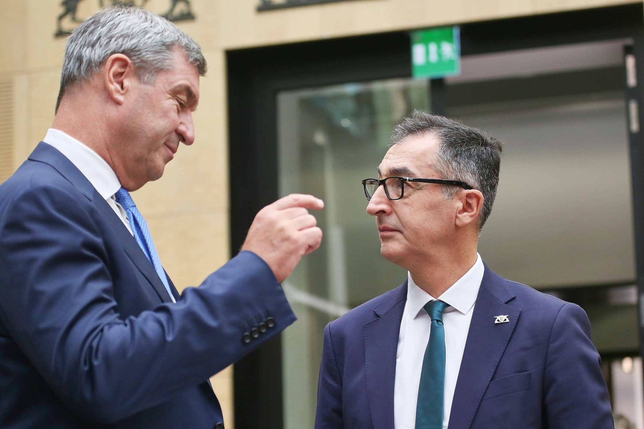 Zwei Männer in Anzügen im Gespräch vor einer Glastür.