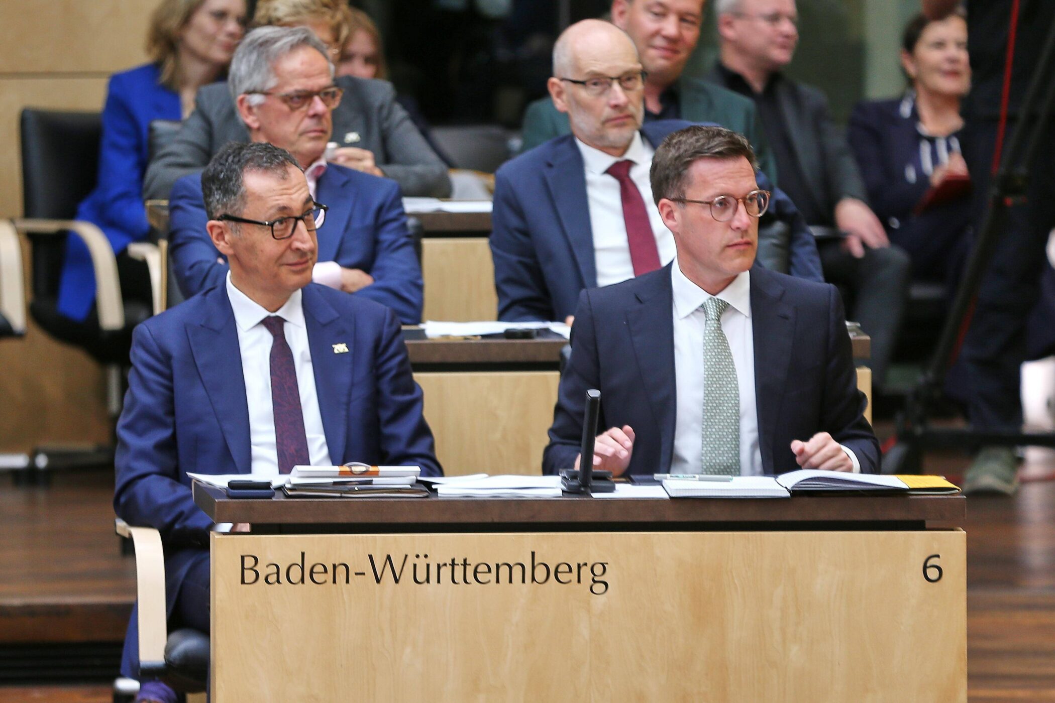 Zwei Männer im Anzug sitzen an einem Tisch mit der Aufschrift "Baden-Württemberg 6".