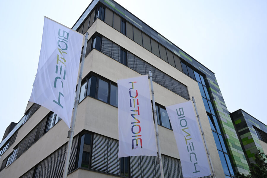 Mehrere weiße Fahnen mit "BIONTECH"-Logo vor modernem Gebäude.