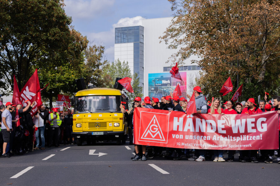 Menschen mit roten Fahnen und Banner "Hände weg von unseren Arbeitsplätzen!"