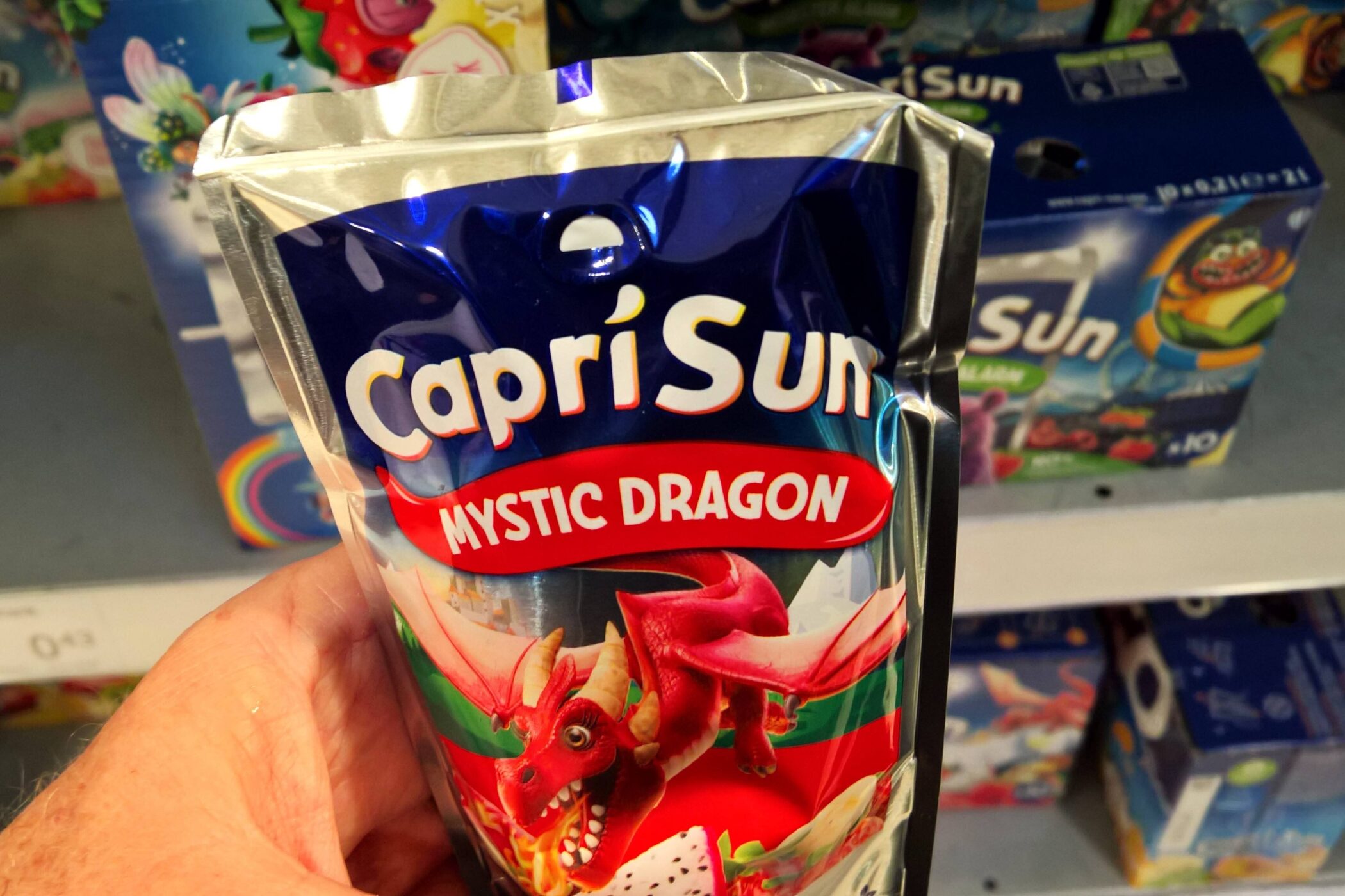 Capri-Sun Tüte mit der Aufschrift "Mystic Dragon" in einer Hand im Supermarkt.