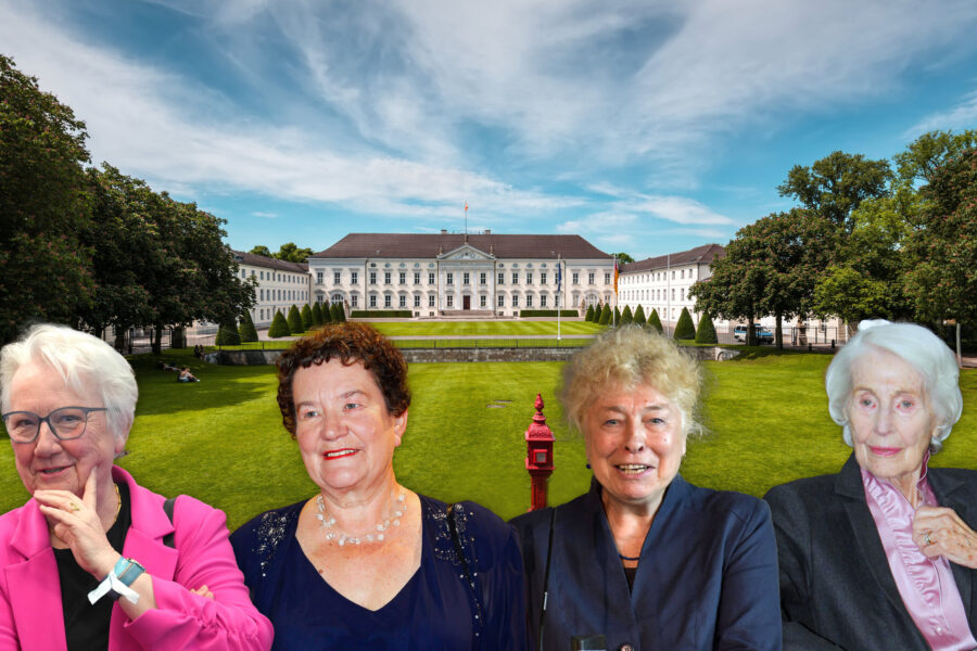 Vier ältere Frauen vor einem großen, weißen Gebäude mit gepflegtem Rasen.